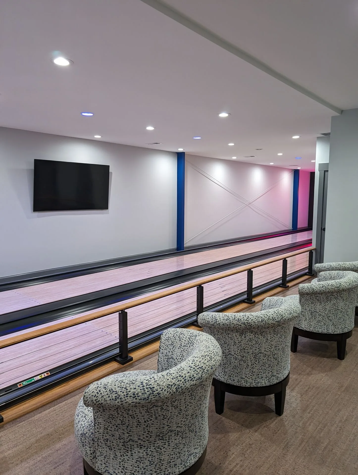 Bowling lane lounge with custom seating, blue accent wall, and wall-mounted television